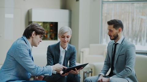 Three professionals discussing a tablet in a modern office.