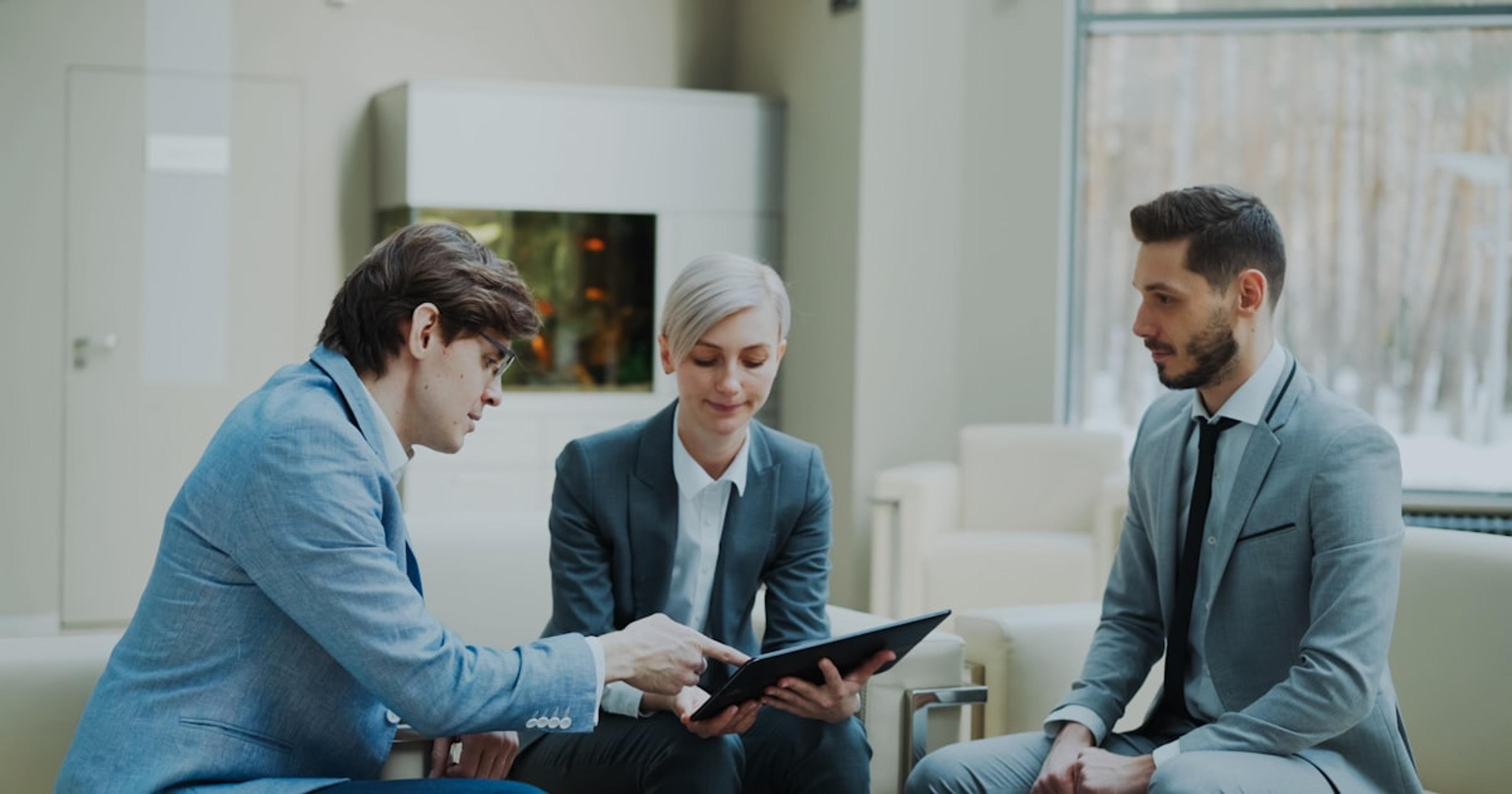 Three professionals discussing a tablet in a modern office.