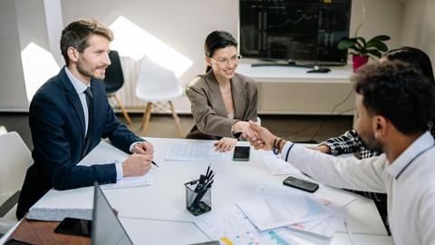 A diverse group of professionals in a business meeting shaking hands and discussing financial charts.