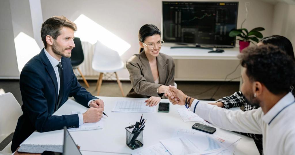 A diverse group of professionals in a business meeting shaking hands and discussing financial charts.