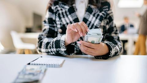 A close-up of a woman counting US dollars in an office environment, symbolizing financial management.