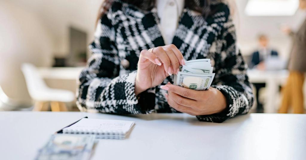 A close-up of a woman counting US dollars in an office environment, symbolizing financial management.