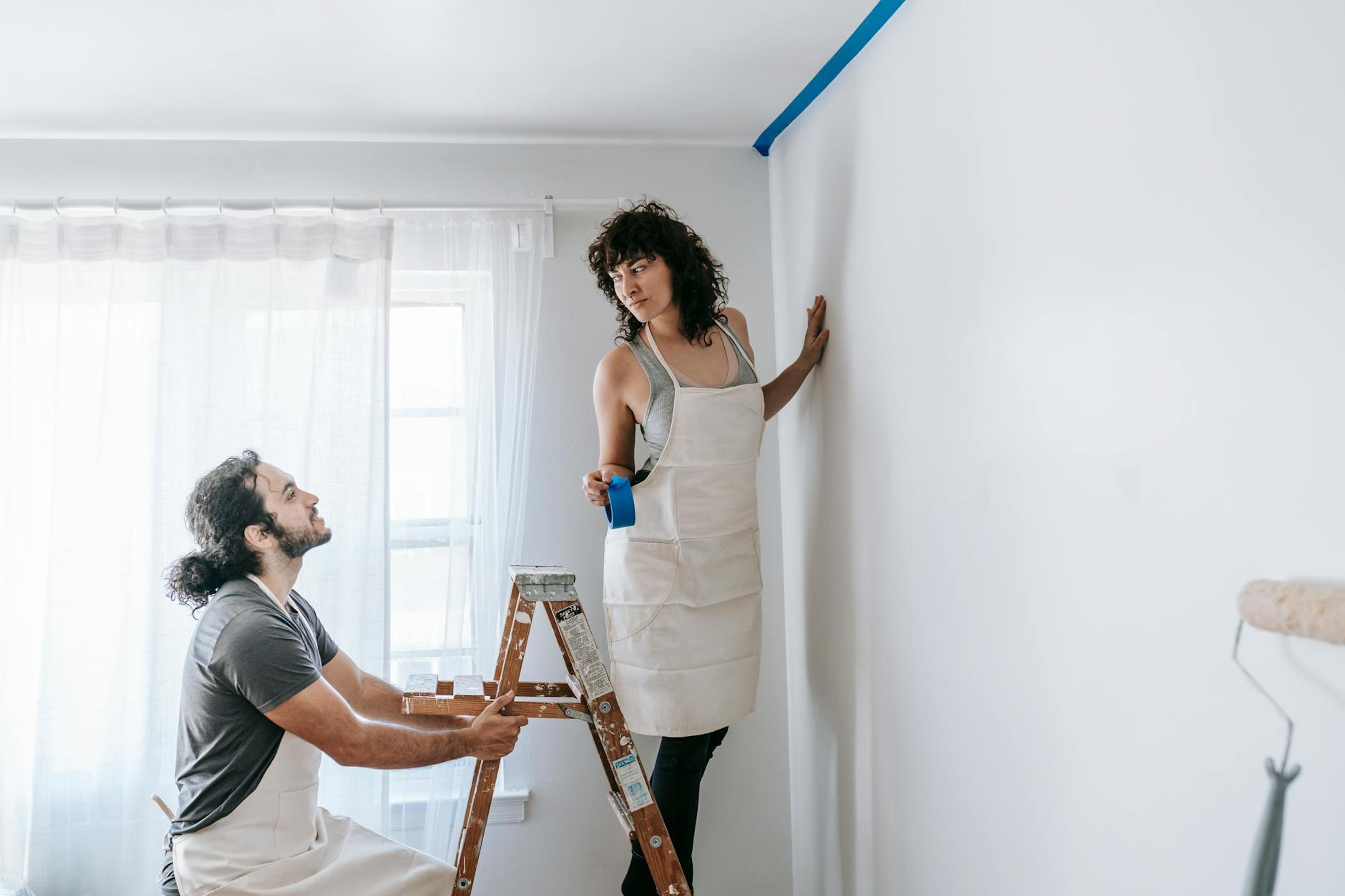 A couple in aprons working together on room renovation using paint rollers indoors.
