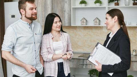 A young couple engaging in a conversation with a real estate agent inside a modern kitchen setting.