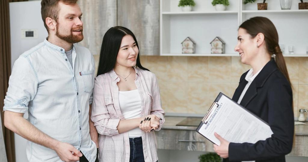 A young couple engaging in a conversation with a real estate agent inside a modern kitchen setting.