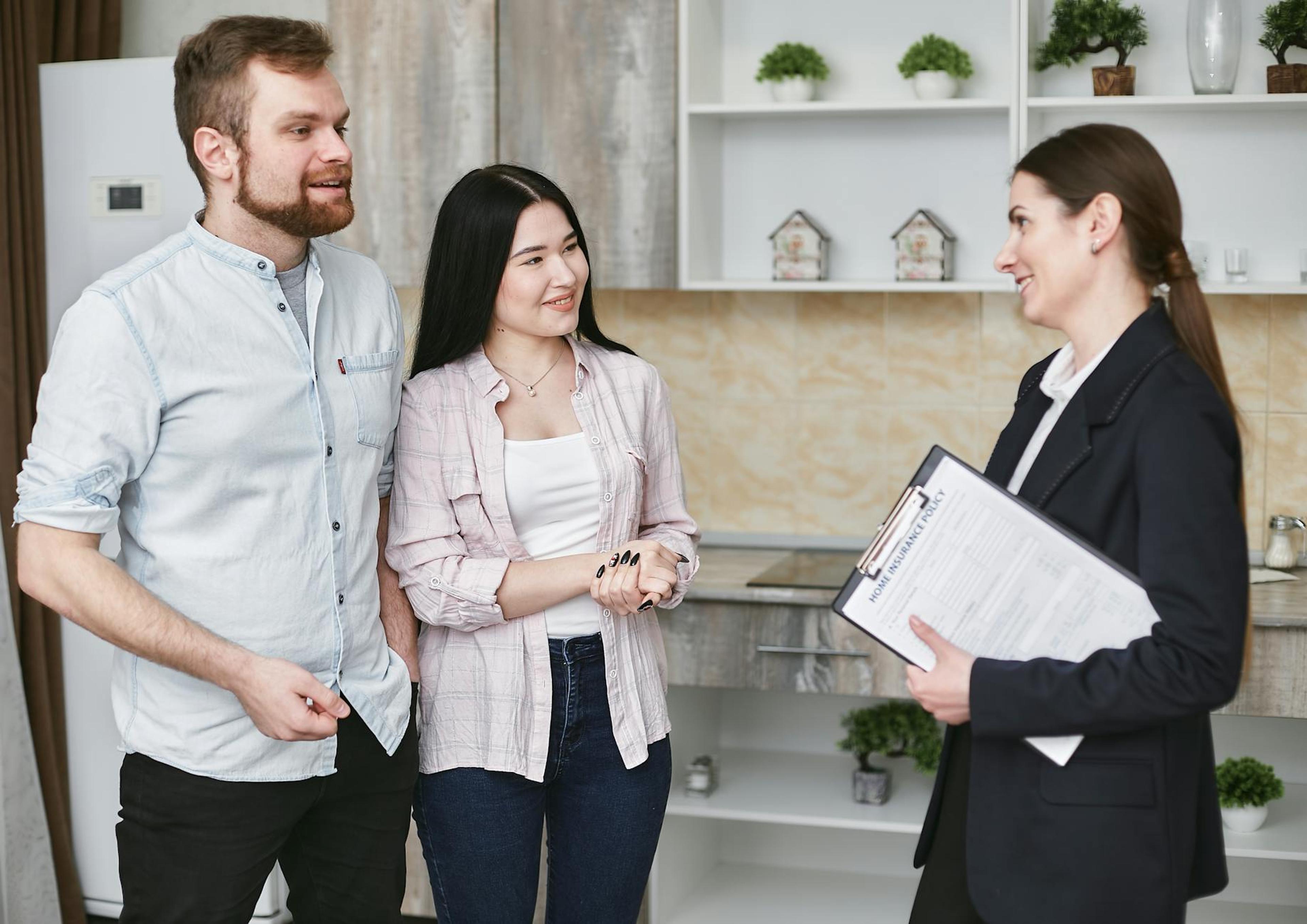 A young couple engaging in a conversation with a real estate agent inside a modern kitchen setting.
