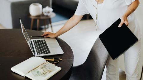 A woman multitasking with a laptop and tablet in a modern office setting.