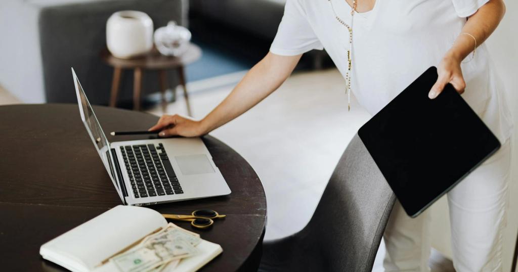 A woman multitasking with a laptop and tablet in a modern office setting.