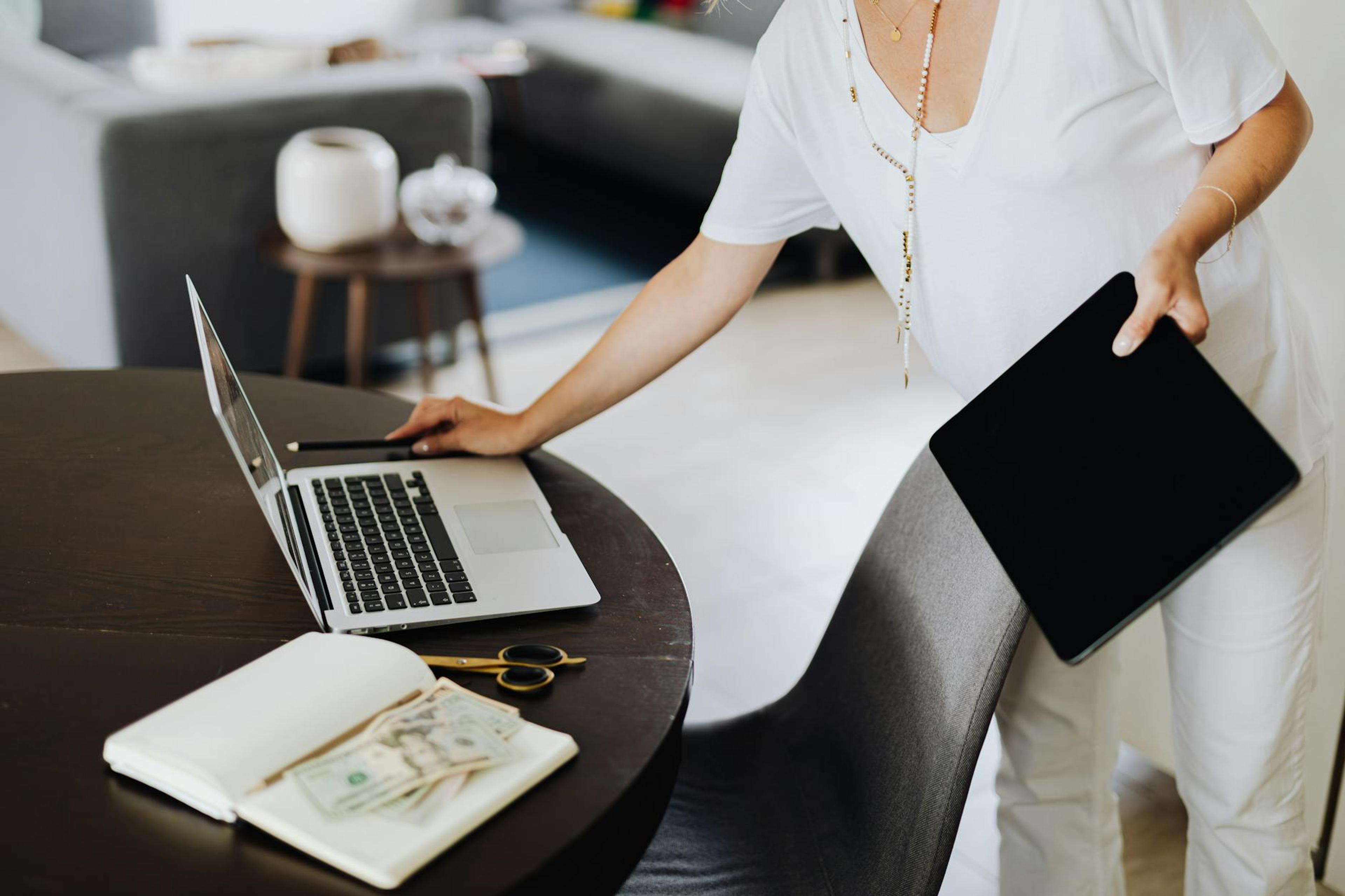 A woman multitasking with a laptop and tablet in a modern office setting.