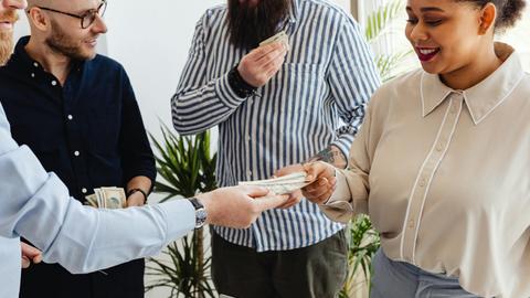 Business professionals exchanging money in a casual office setting.
