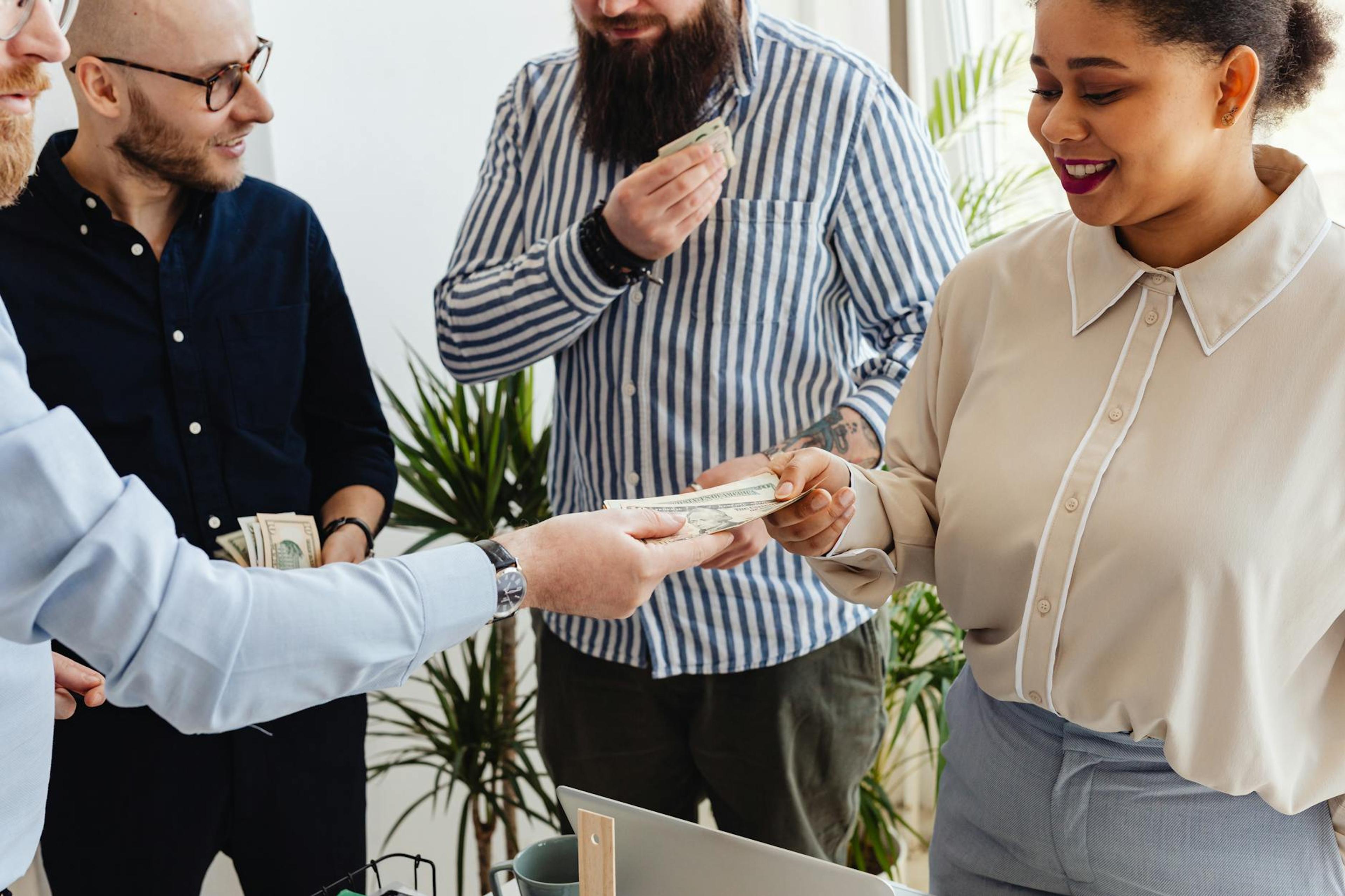 Business professionals exchanging money in a casual office setting.