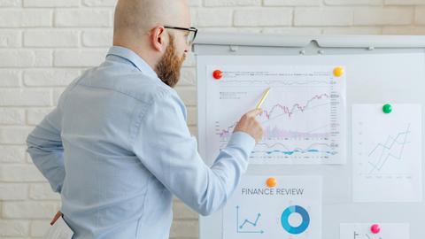 Bald businessman in office analyzes graphs on whiteboard, indicating finance trends.