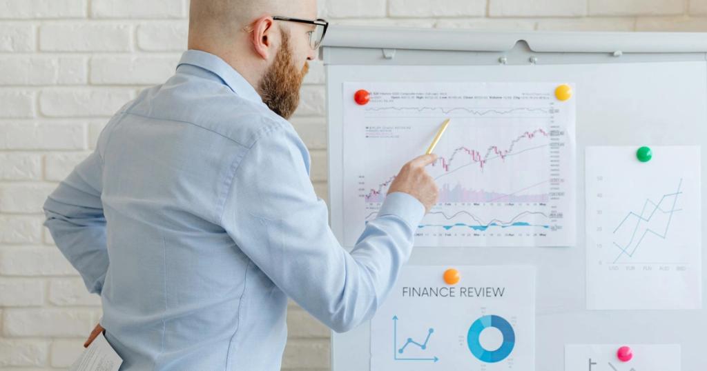 Bald businessman in office analyzes graphs on whiteboard, indicating finance trends.