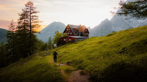 A person hikes towards a house in the mountains.