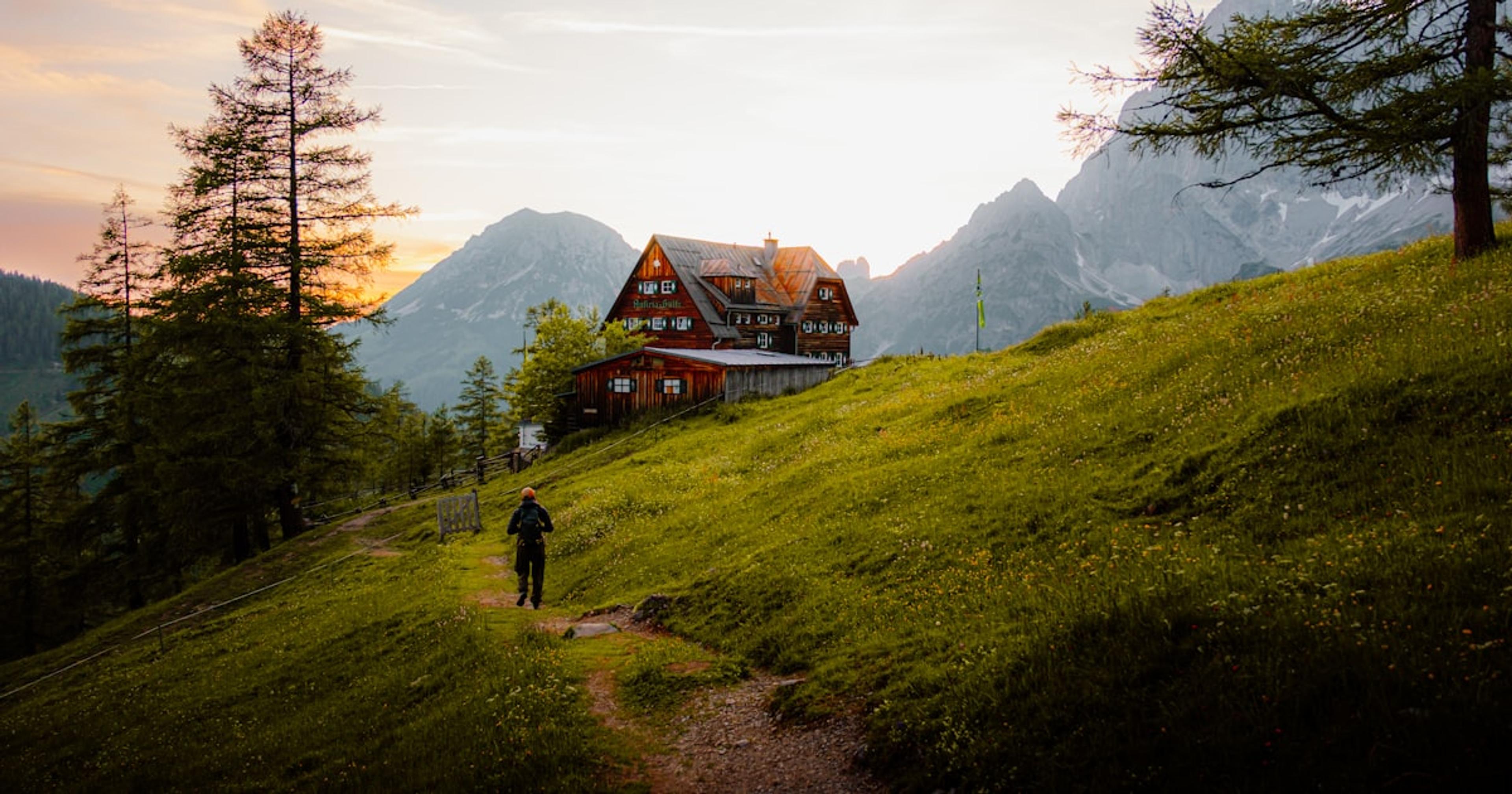 A person hikes towards a house in the mountains.