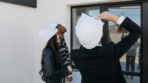 Real estate agents wearing hard hats inspect a property's exterior, assessing potential investments.