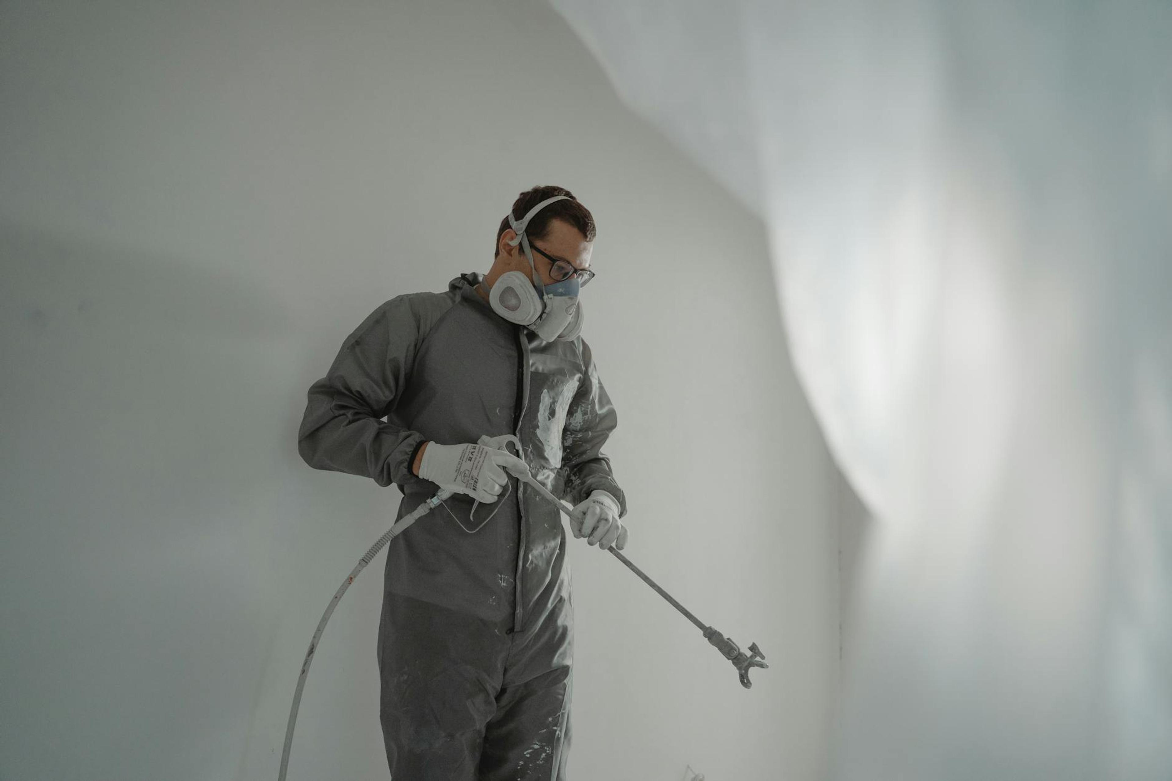 Person in protective gear painting a wall, showcasing house renovation work.