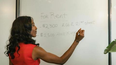 Professional woman writing real estate prices on a whiteboard for rental properties.