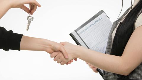 A real estate transaction with a handshake and key exchange, highlighting a home insurance document.