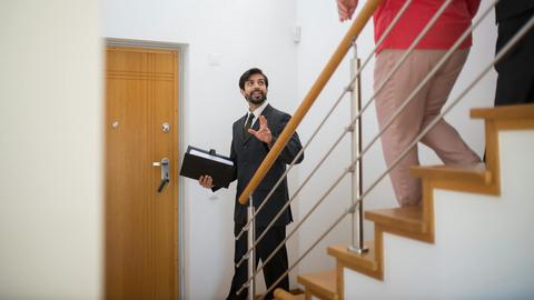 A realtor conducting a house tour with potential buyers on the stairs of a modern home.