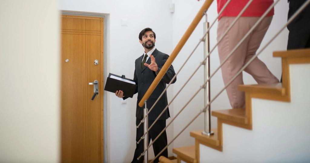 A realtor conducting a house tour with potential buyers on the stairs of a modern home.