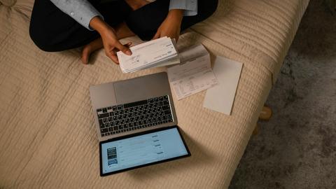 Overhead view of woman organizing finances on bed with laptop and checks.