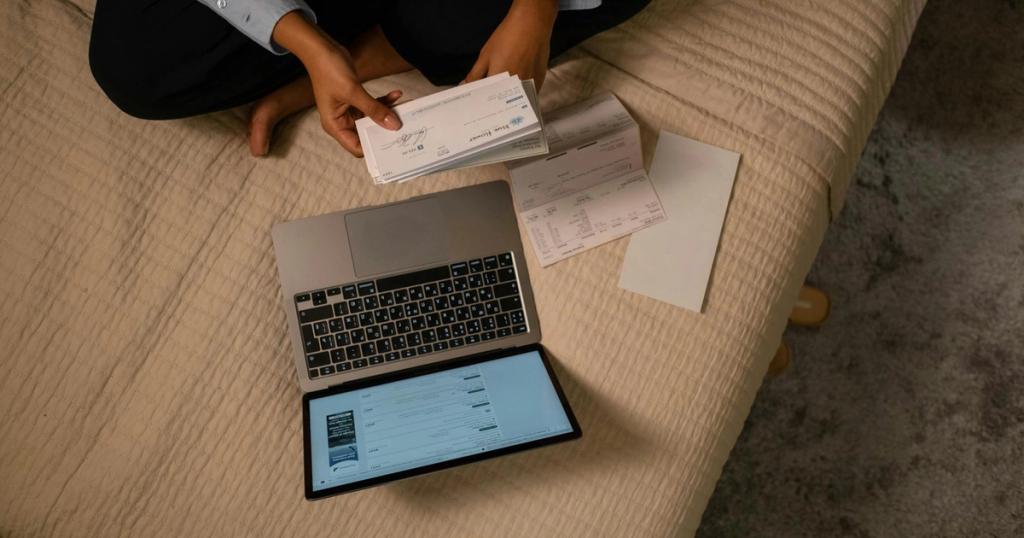 Overhead view of woman organizing finances on bed with laptop and checks.
