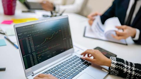 Business team analyzes cryptocurrency market trends using a laptop with graphs and data.