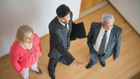 A realtor shows a property to a senior couple in a modern indoor setting.