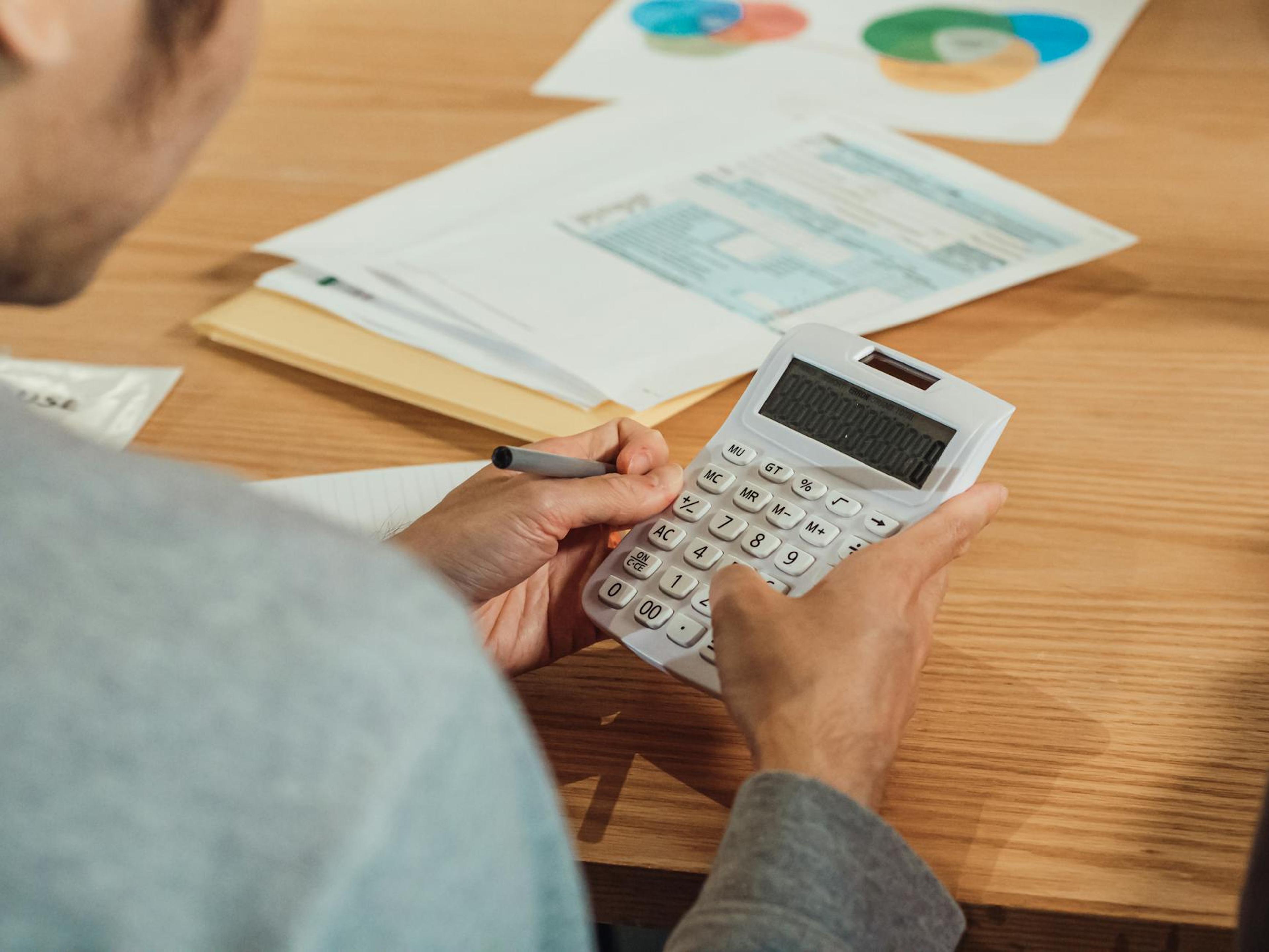 Person using a calculator at a desk with financial documents. Modern business concept.