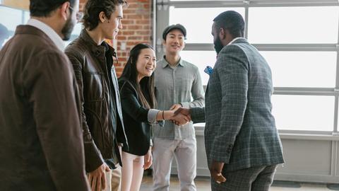 A diverse group of business professionals engaging in a handshake and discussion in a modern office space.