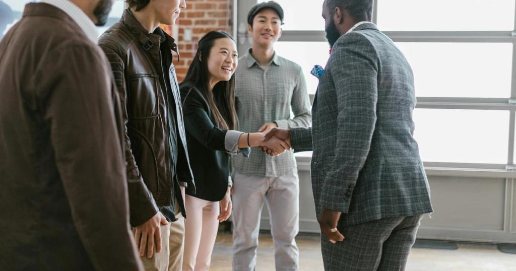 A diverse group of business professionals engaging in a handshake and discussion in a modern office space.