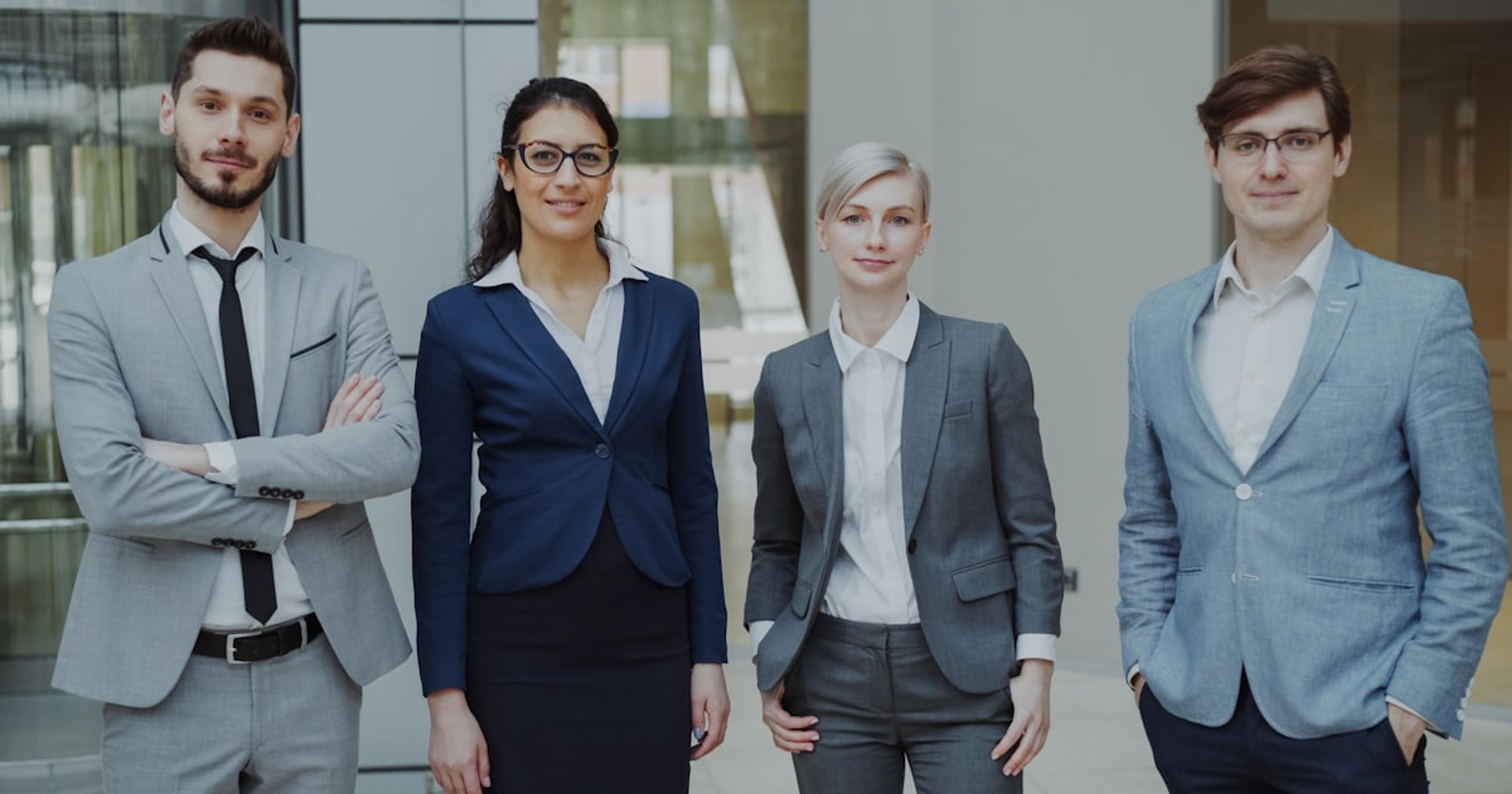 Four business professionals standing together indoors.
