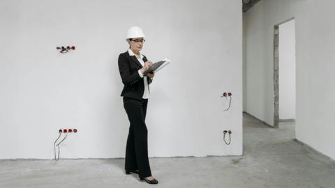 Woman in hard hat reviews notes at a construction site, examining progress.