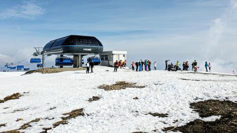 A group of skiers preparing near a modern chairlift station on a snowy mountain under a clear blue sky.