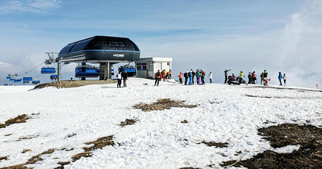 A group of skiers preparing near a modern chairlift station on a snowy mountain under a clear blue sky.