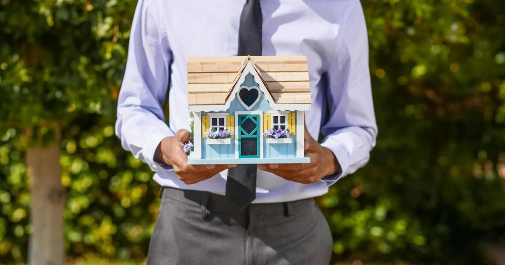 A business professional holds a decorative miniature house, symbolizing real estate investment.