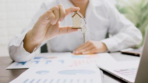 Real estate professional presenting a house model with keys, symbolizing property investment and ownership.