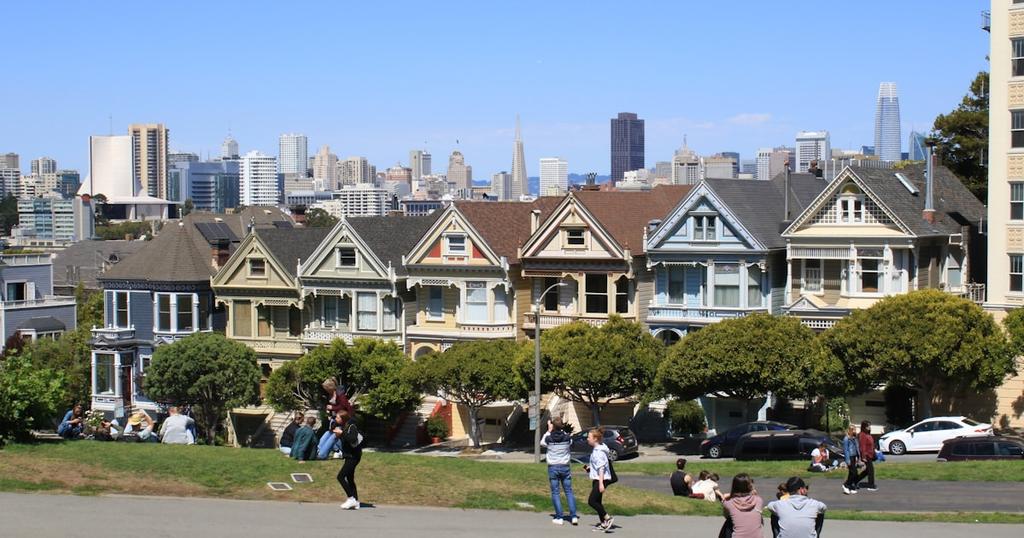 a group of people sitting on the grass in front of a row of houses