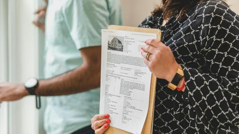 Real estate agent holding property documents on a clipboard in an office setting.