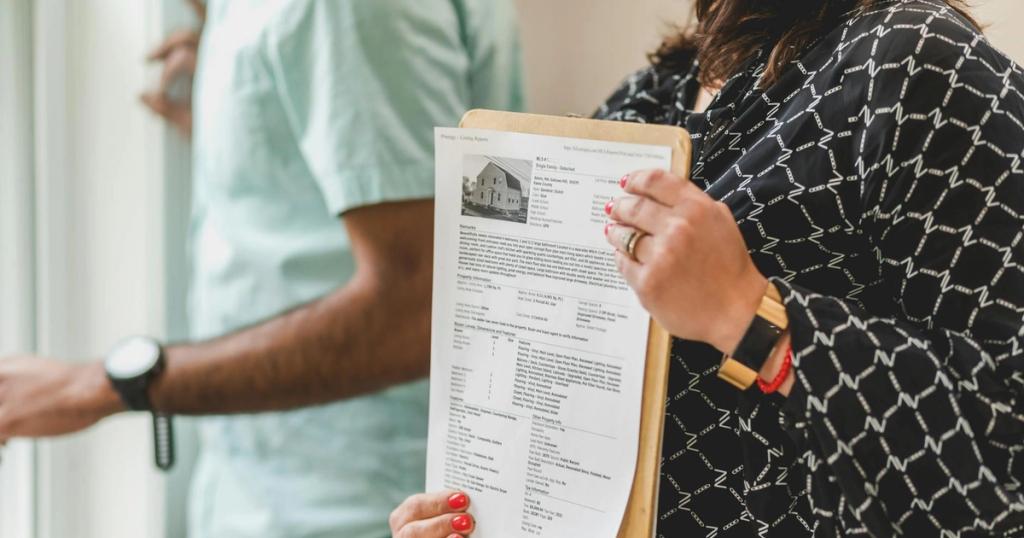 Real estate agent holding property documents on a clipboard in an office setting.