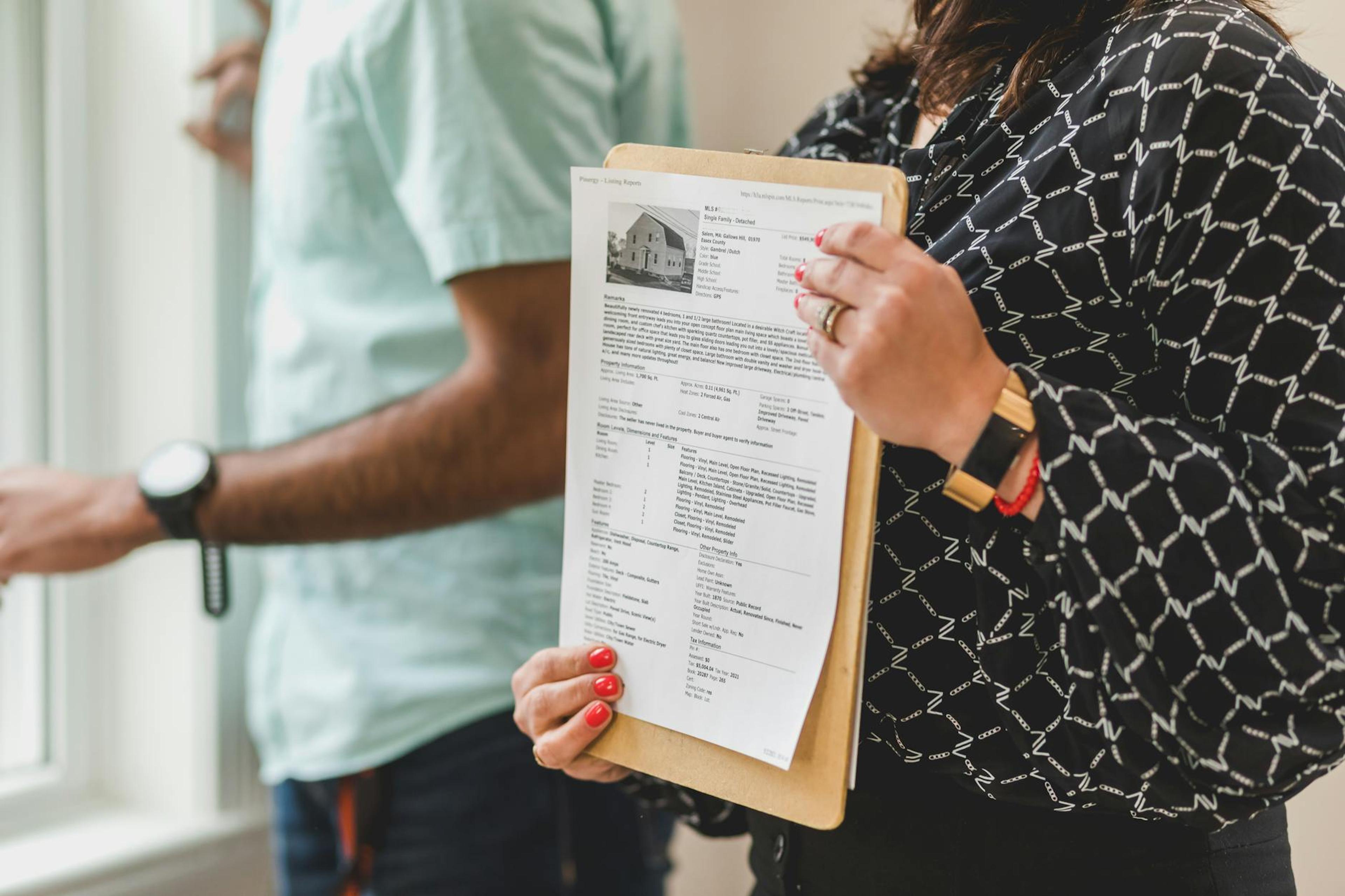 Real estate agent holding property documents on a clipboard in an office setting.