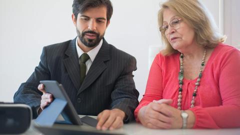 Business meeting in Portugal between a man and senior woman discussing with tablet.