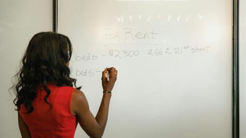 Professional woman in red dress writing real estate information on a whiteboard.