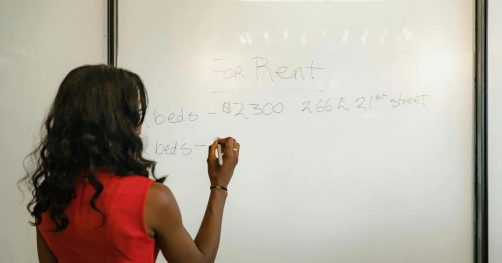 Professional woman in red dress writing real estate information on a whiteboard.