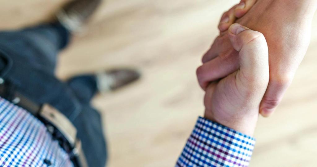 Close-up of a handshake between two people inside an office, symbolizing trust and cooperation.