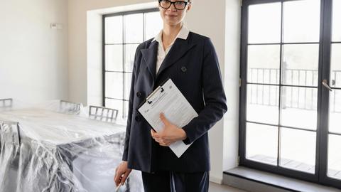 Confident real estate agent standing indoors holding property documents.