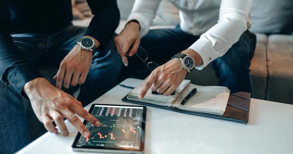 Two businessmen pointing at stock market data on a tablet, engaged in discussion.