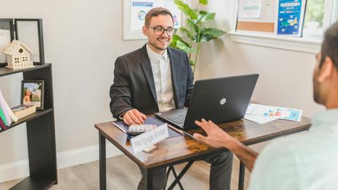 Mortgage broker in an office meeting with a client, utilizing a laptop.