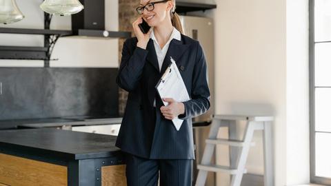 Confident businesswoman in office attire making a call while holding a clipboard in a modern workspace.